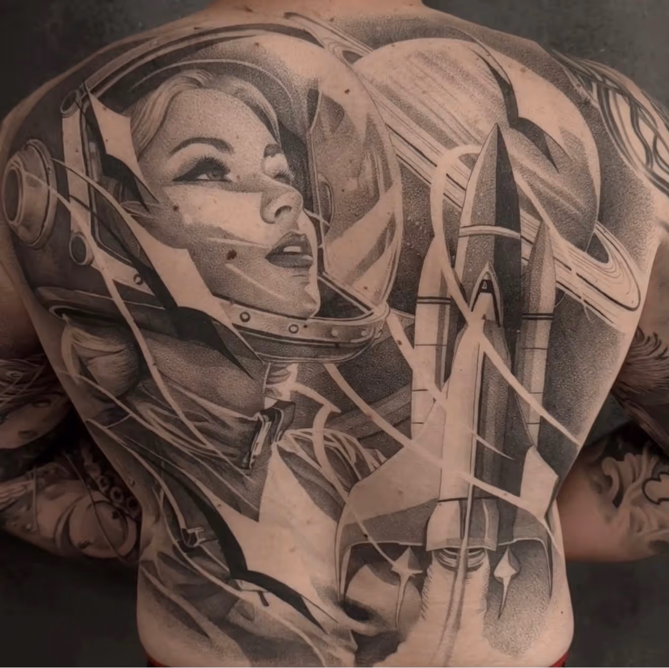 Detailed full sleeve tattoo of a large grinning face with a protruding tongue, a snarling wolf skull, a castle, and a grim reaper skull on a person's arm.