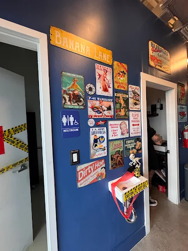 Blue wall decorated with vintage-style metal signs including 'BANANA LANE', restroom sign, P-40 Warhawk plane, and humorous themed posters near two doorways.