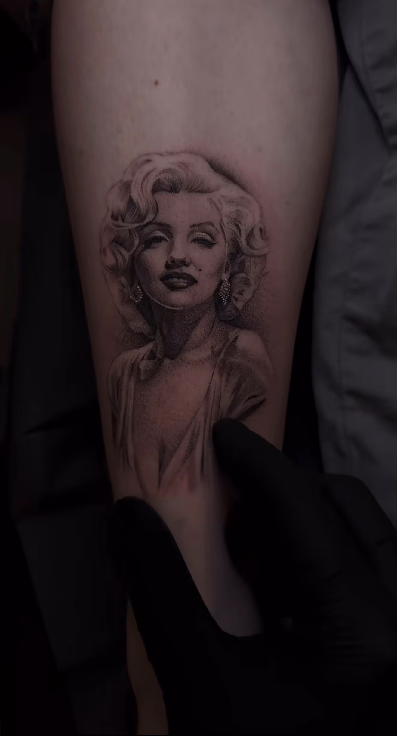 Detailed full sleeve tattoo of a large grinning face with a protruding tongue, a snarling wolf skull, a castle, and a grim reaper skull on a person's arm.