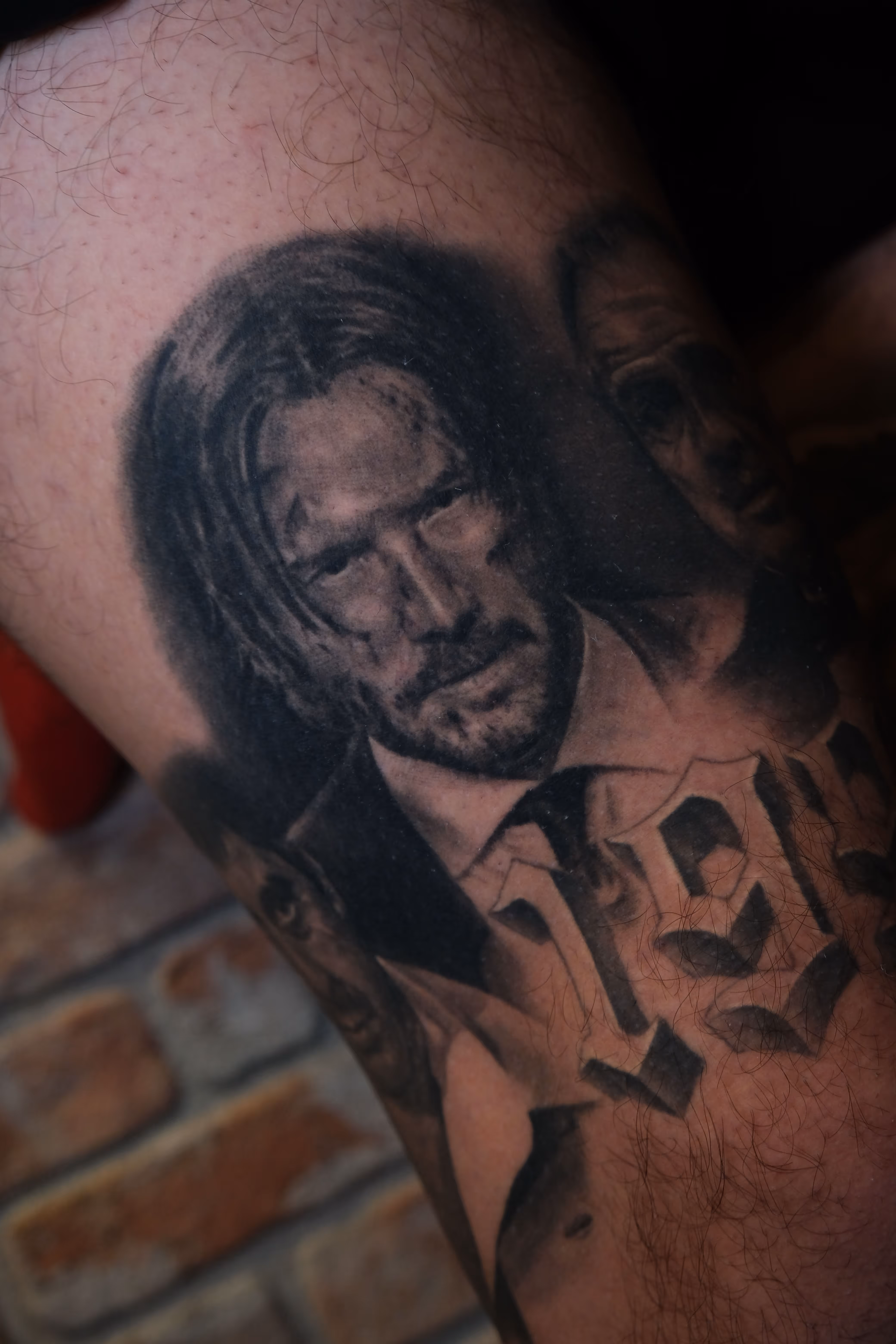 Detailed full sleeve tattoo of a large grinning face with a protruding tongue, a snarling wolf skull, a castle, and a grim reaper skull on a person's arm.