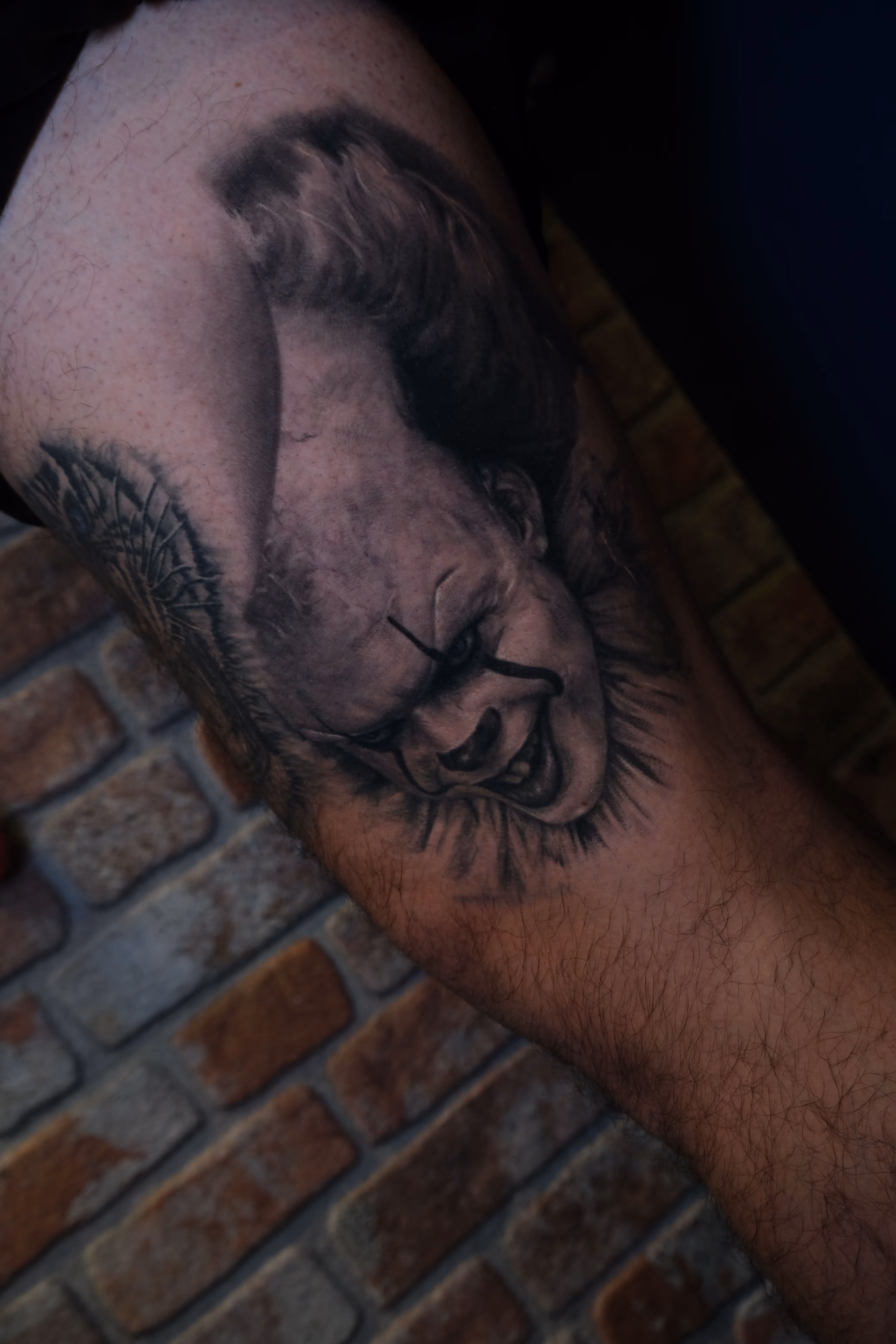 Detailed full sleeve tattoo of a large grinning face with a protruding tongue, a snarling wolf skull, a castle, and a grim reaper skull on a person's arm.