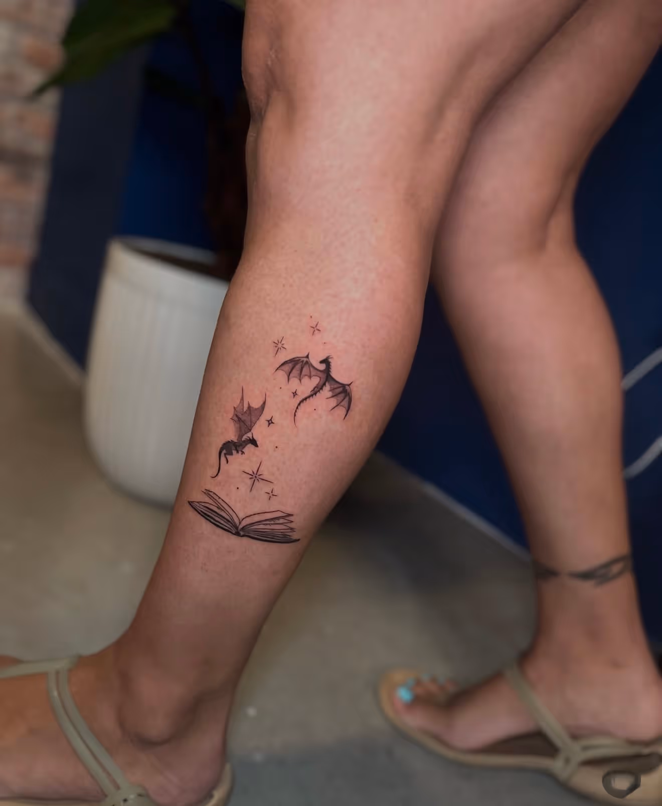 Detailed full sleeve tattoo of a large grinning face with a protruding tongue, a snarling wolf skull, a castle, and a grim reaper skull on a person's arm.