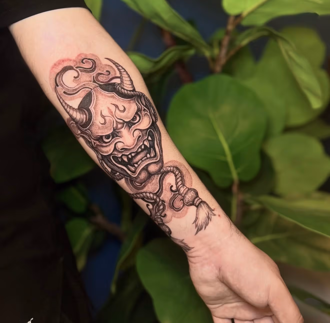 Detailed full sleeve tattoo of a large grinning face with a protruding tongue, a snarling wolf skull, a castle, and a grim reaper skull on a person's arm.