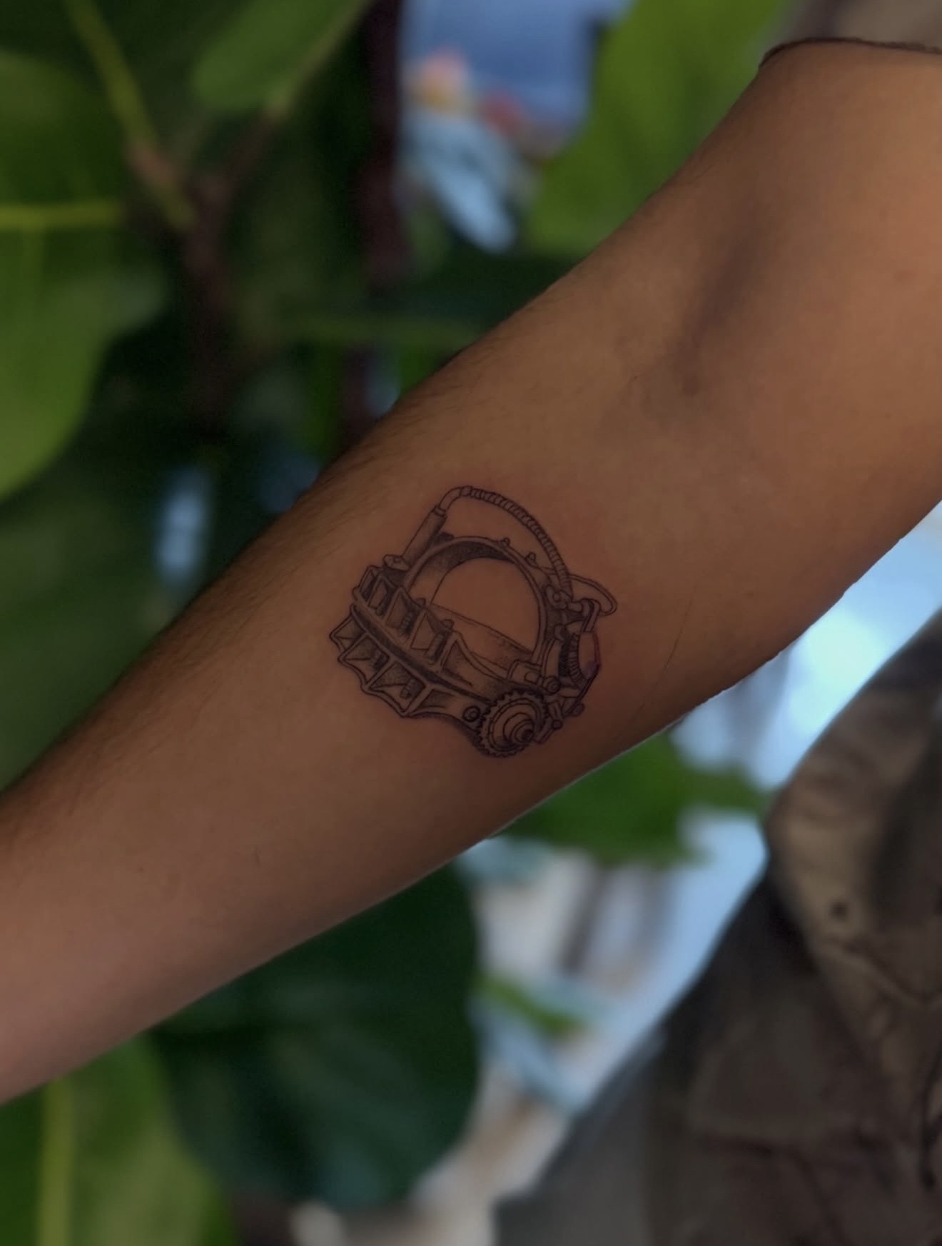 Detailed full sleeve tattoo of a large grinning face with a protruding tongue, a snarling wolf skull, a castle, and a grim reaper skull on a person's arm.
