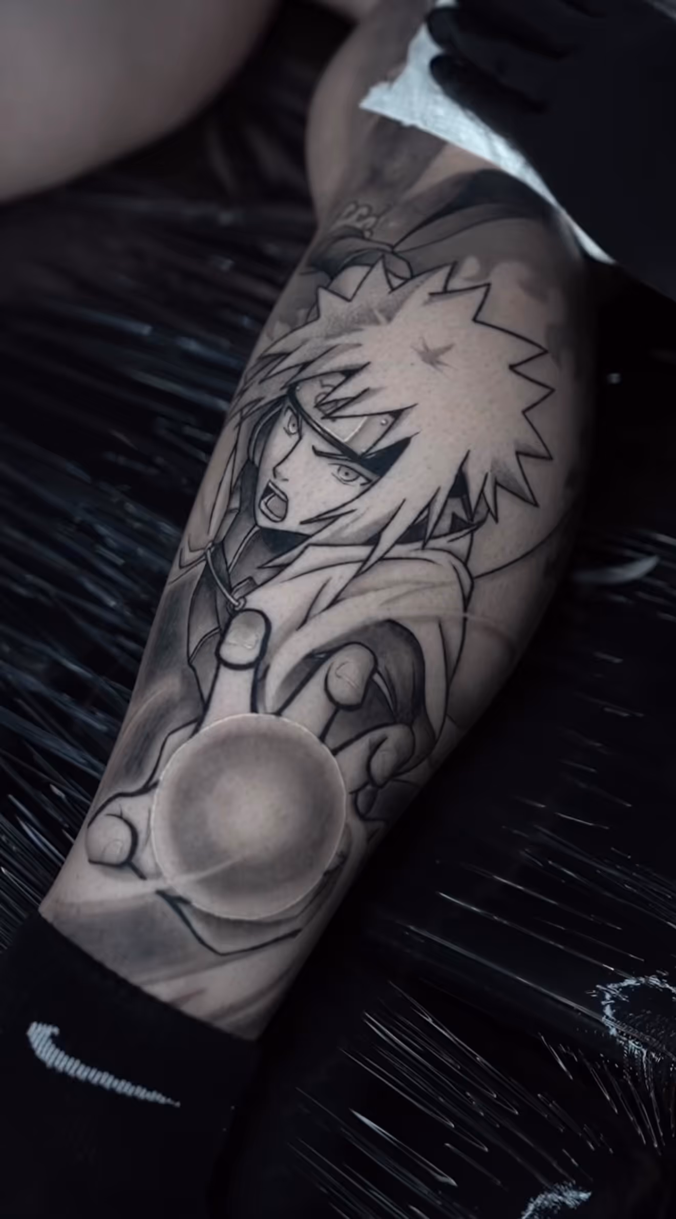 Detailed full sleeve tattoo of a large grinning face with a protruding tongue, a snarling wolf skull, a castle, and a grim reaper skull on a person's arm.