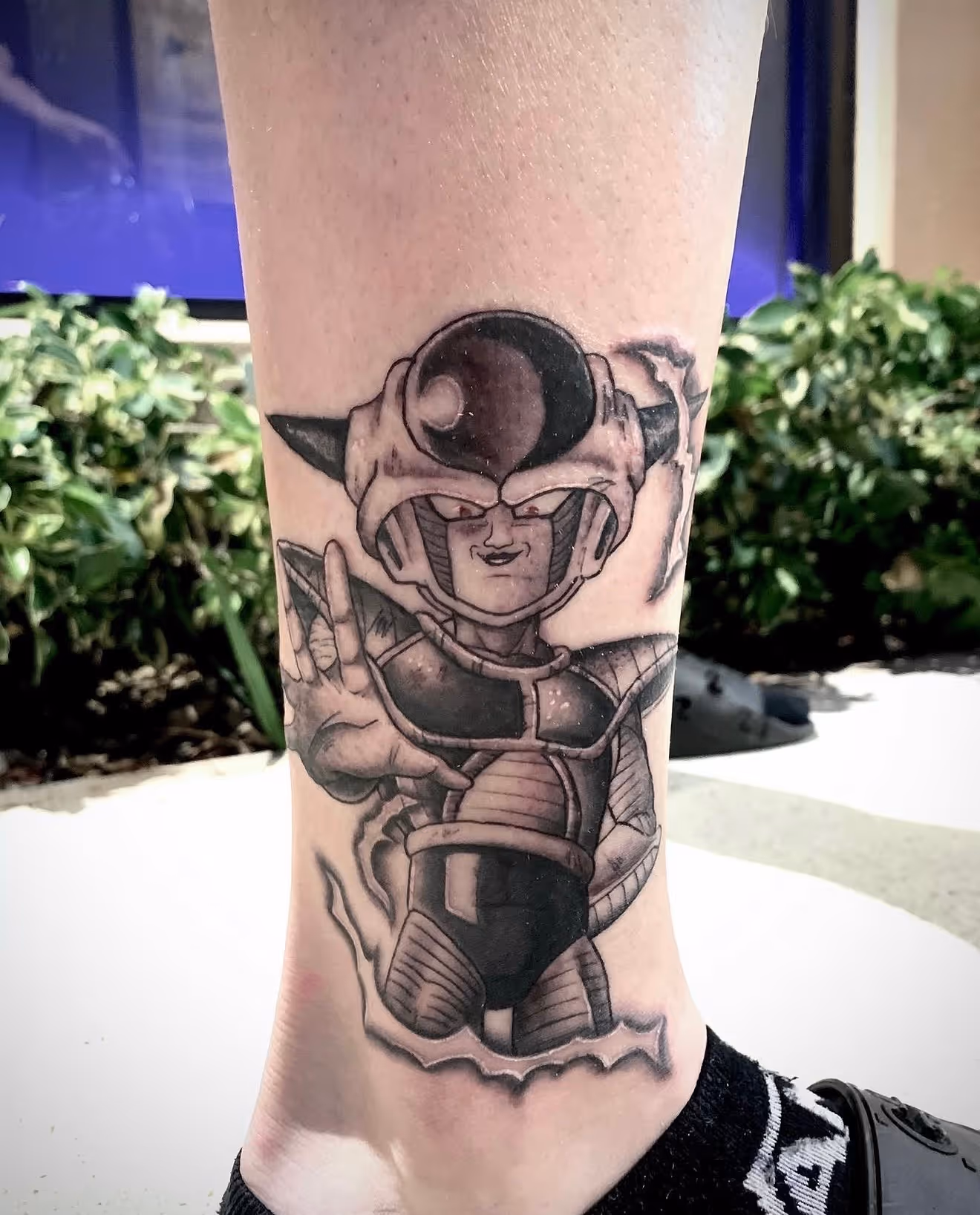 Detailed full sleeve tattoo of a large grinning face with a protruding tongue, a snarling wolf skull, a castle, and a grim reaper skull on a person's arm.