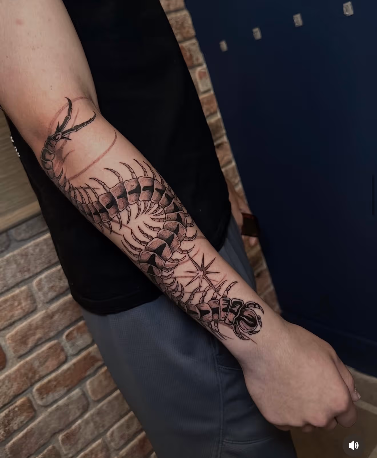 Detailed full sleeve tattoo of a large grinning face with a protruding tongue, a snarling wolf skull, a castle, and a grim reaper skull on a person's arm.