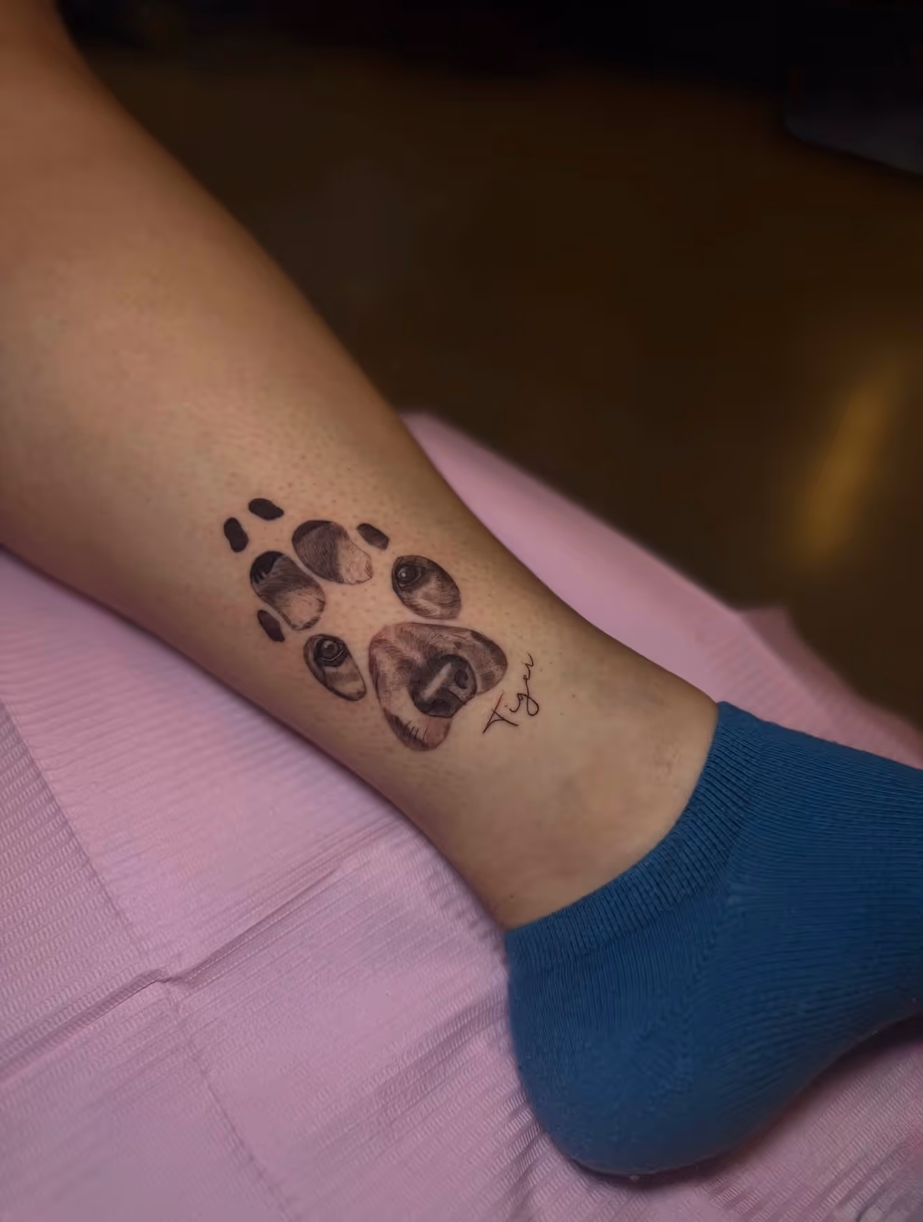 Detailed full sleeve tattoo of a large grinning face with a protruding tongue, a snarling wolf skull, a castle, and a grim reaper skull on a person's arm.