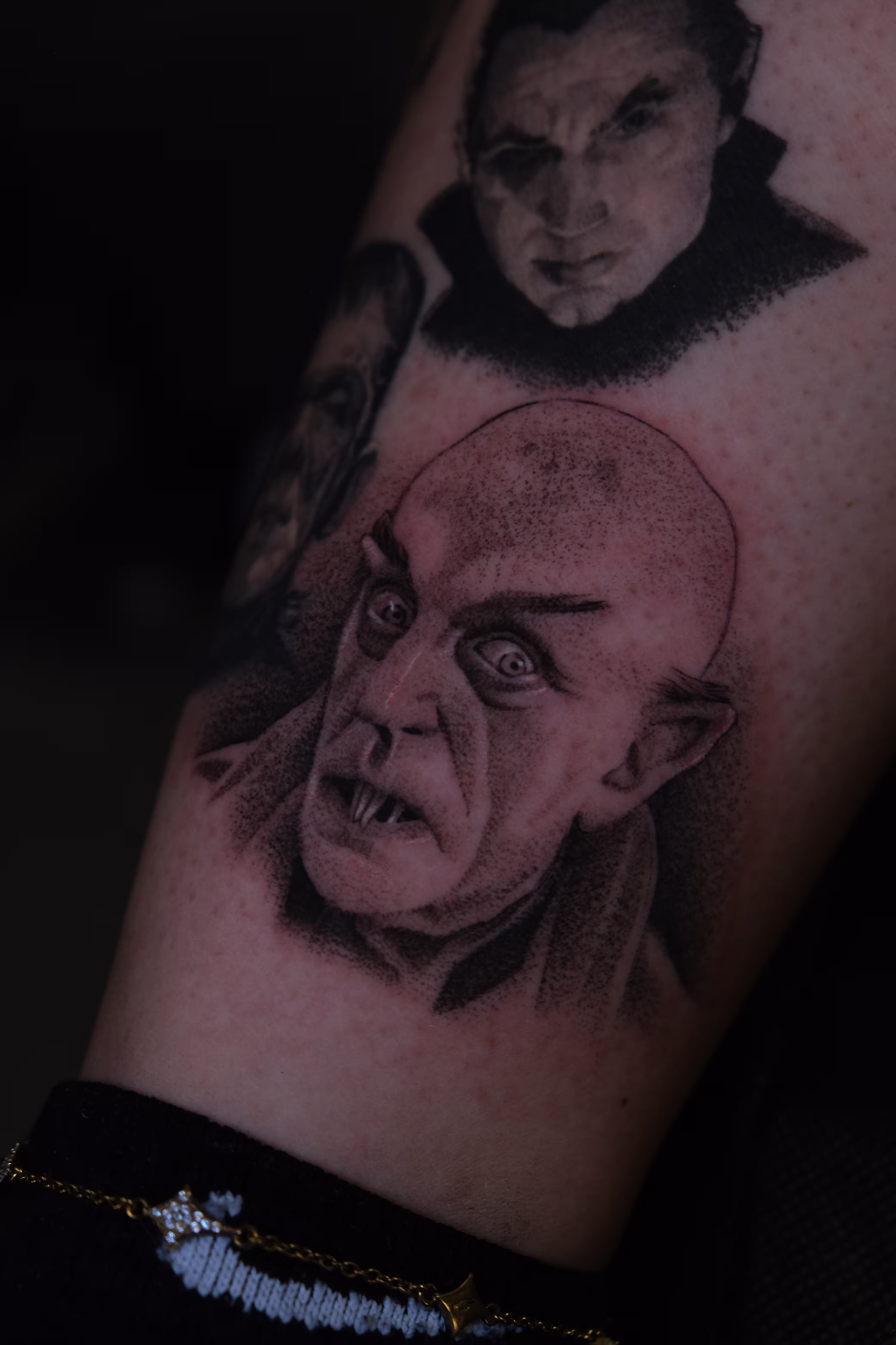 Detailed full sleeve tattoo of a large grinning face with a protruding tongue, a snarling wolf skull, a castle, and a grim reaper skull on a person's arm.