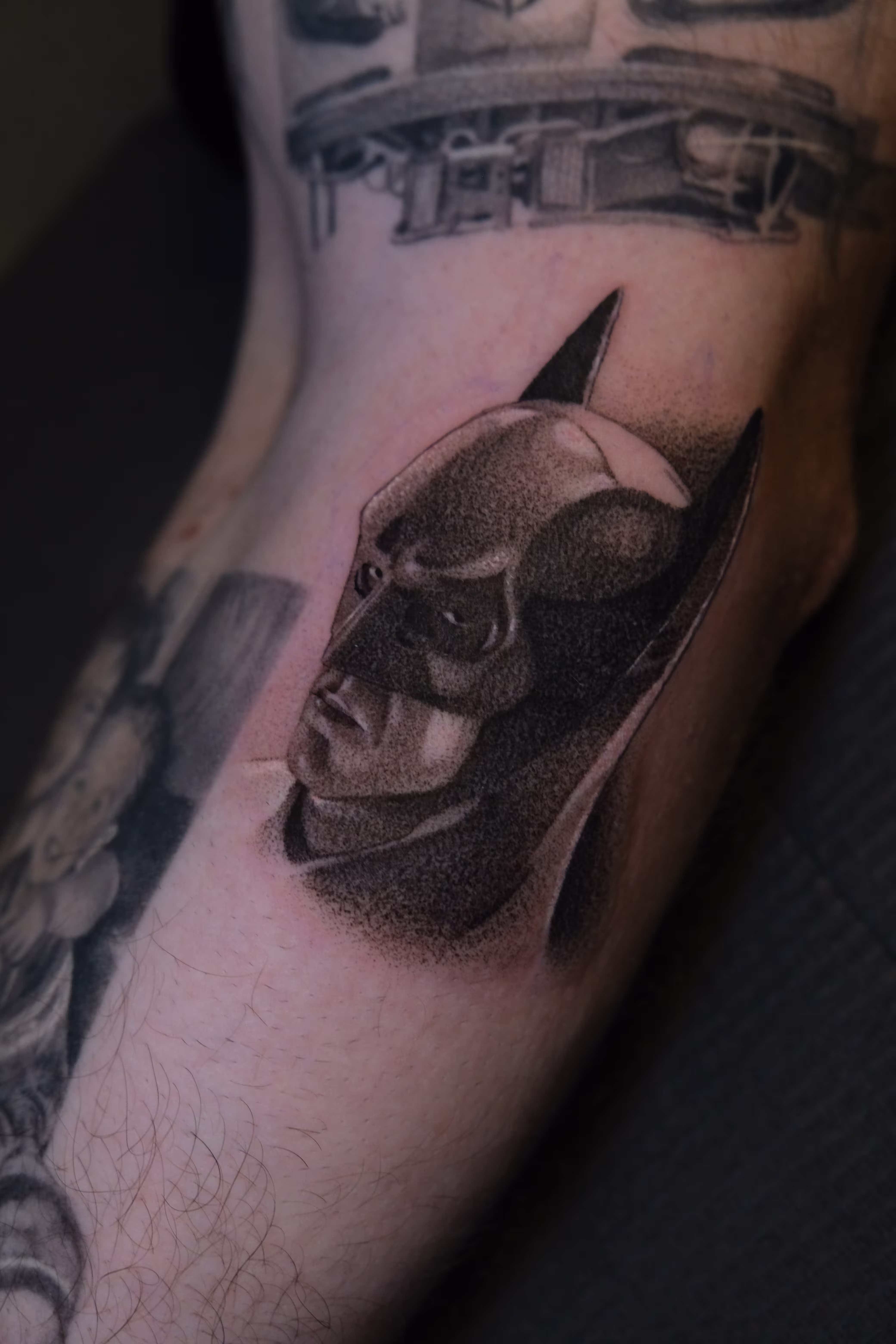 Detailed full sleeve tattoo of a large grinning face with a protruding tongue, a snarling wolf skull, a castle, and a grim reaper skull on a person's arm.