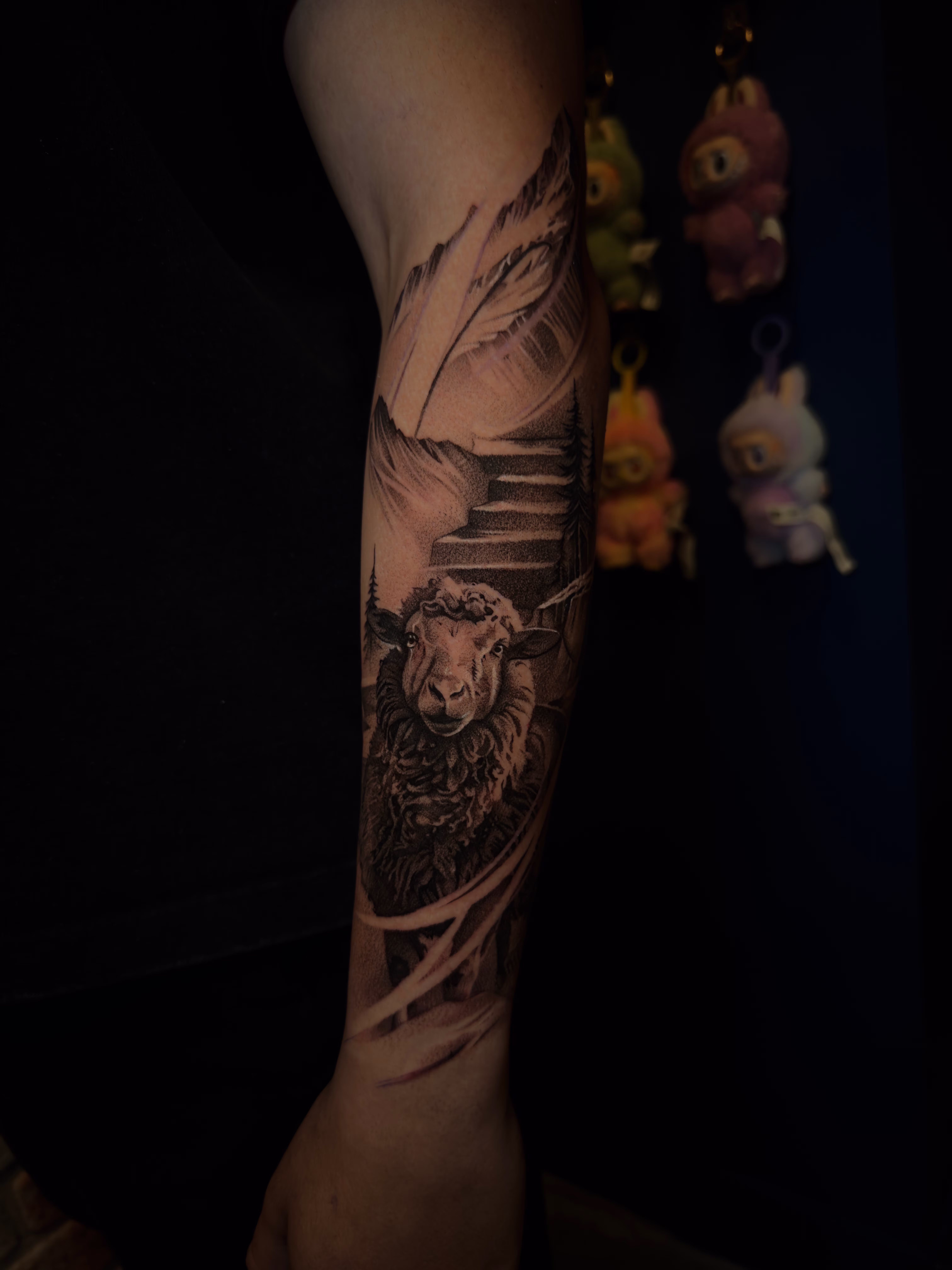Detailed full sleeve tattoo of a large grinning face with a protruding tongue, a snarling wolf skull, a castle, and a grim reaper skull on a person's arm.