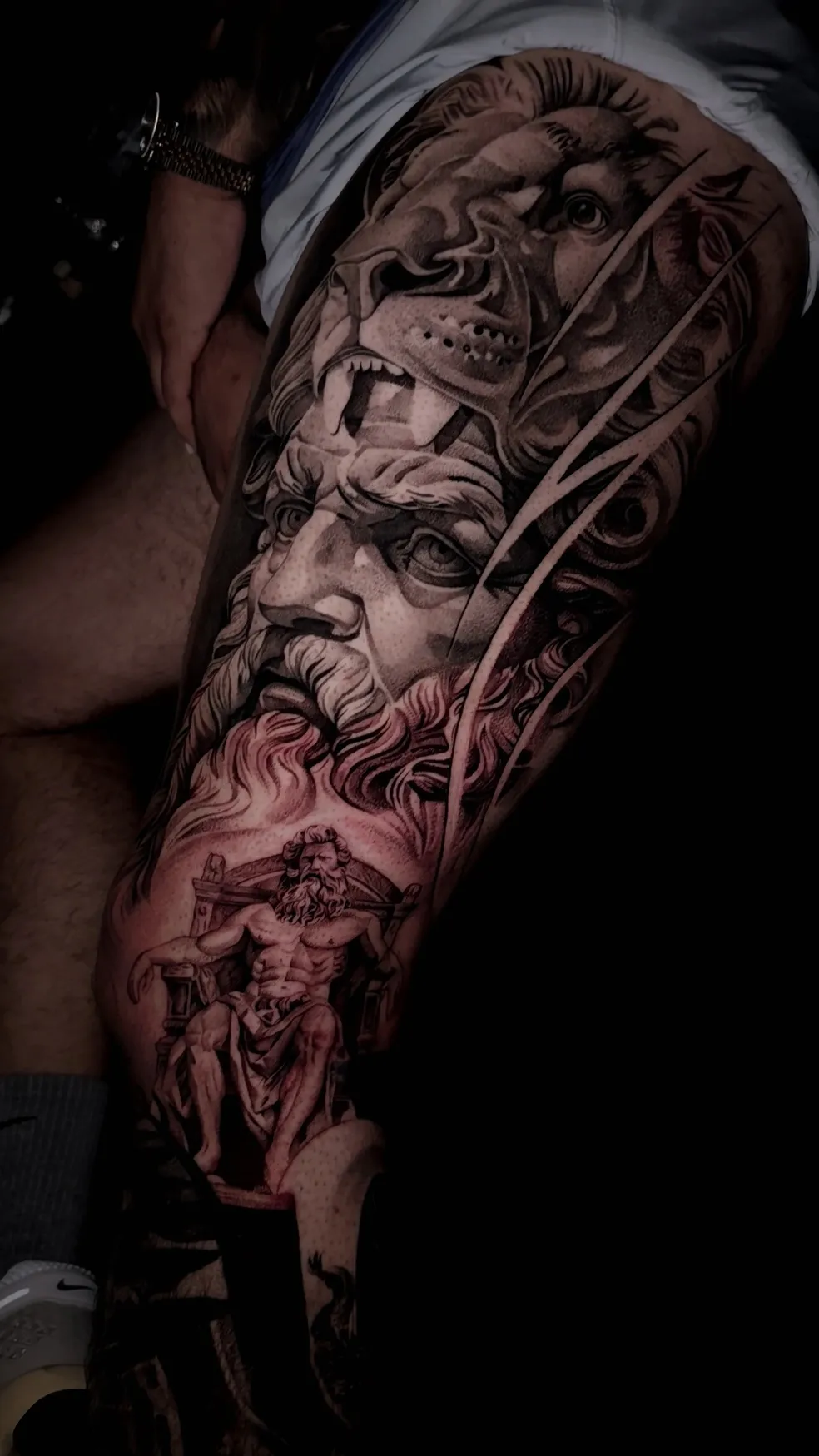 Black and gray tattoo on upper arm depicting a basketball hoop with net, a basketball going through the net, and a pair of Nike sneakers.