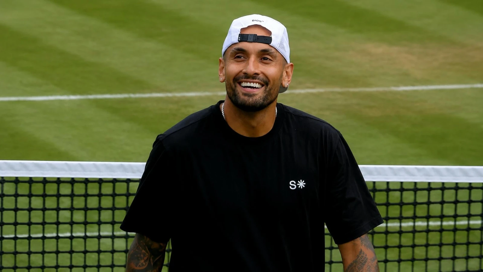 Nick Kyrgios smiling at the net on a grass tennis court