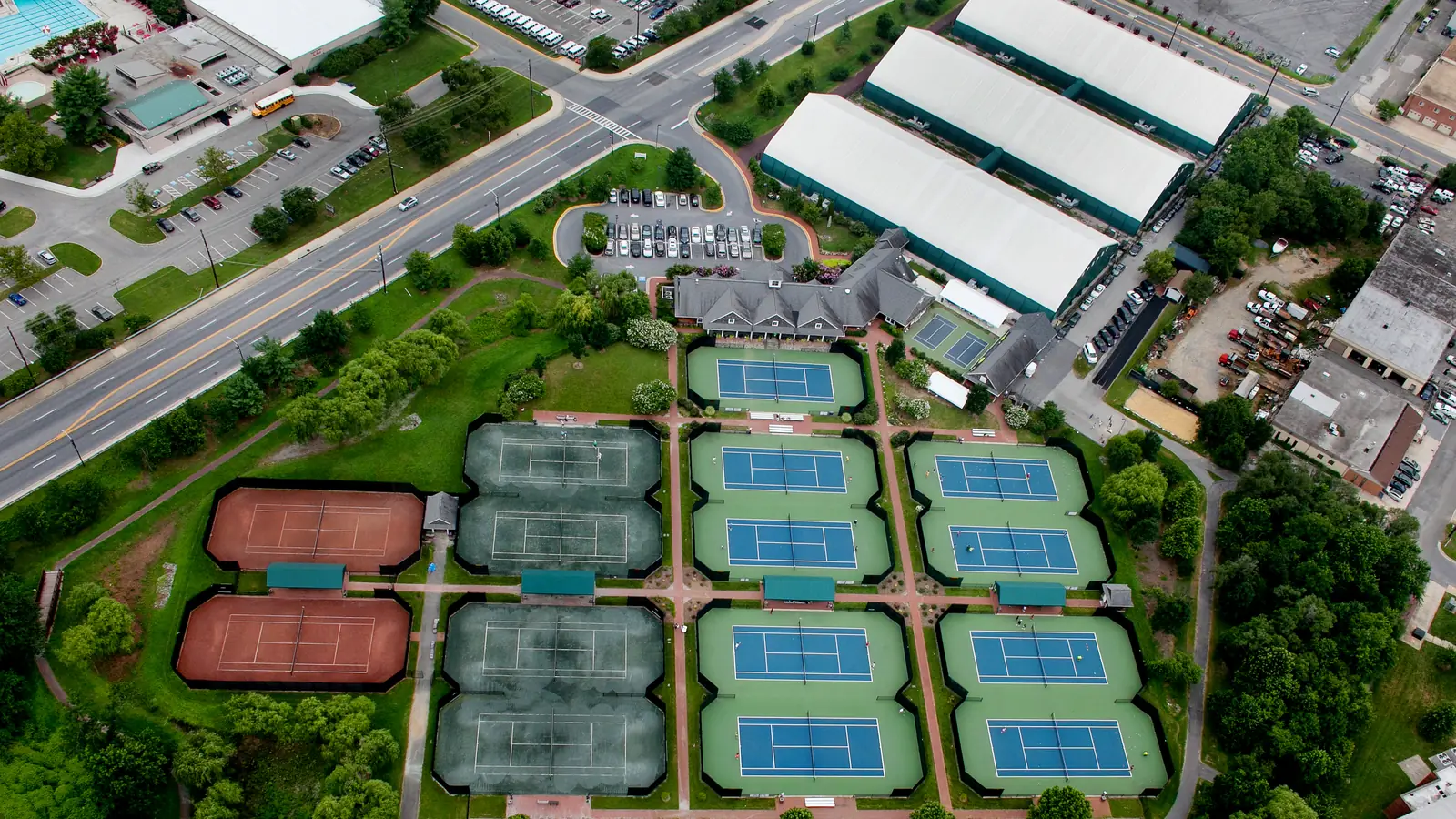 Aerial view of JTCC's College Park campus: rows of hard, Har-Tru and red clay courts beside its indoor tennis buildings