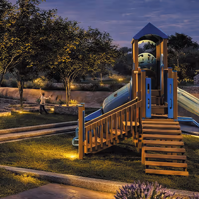 Área de juegos iluminada al atardecer con toboganes azules y estructura de madera en un parque.