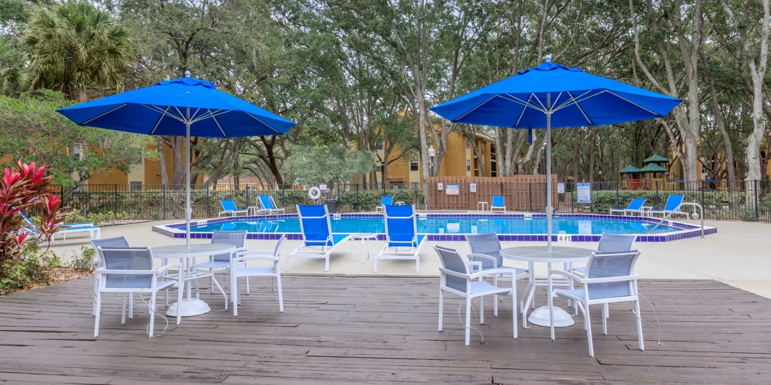 Swimming pool with trees, lounge chairs and tables with umbrellas