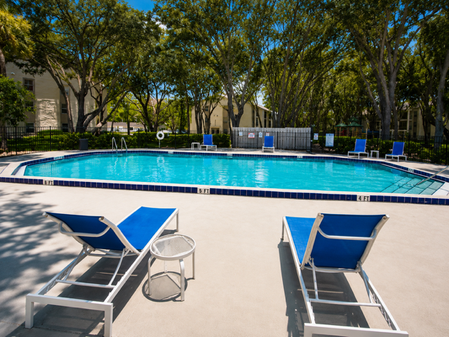 Swimming pool with trees, lounge chairs and tables with umbrellas