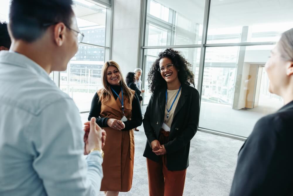 Group of colleagues engaging in networking at a corporate event, sharing laughter and socializing in a modern office environment.