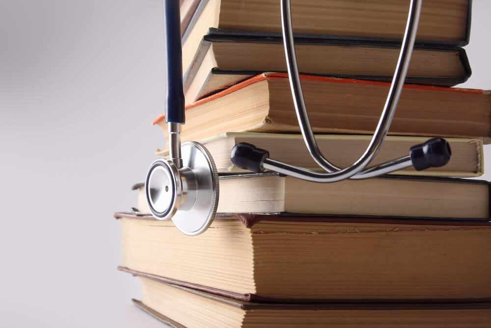 Stethoscope on pile of books isolated. Blue background