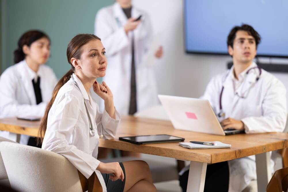 Interested medic student or doctor sitting at table discussing ideas and watching presentation during meeting in bright office