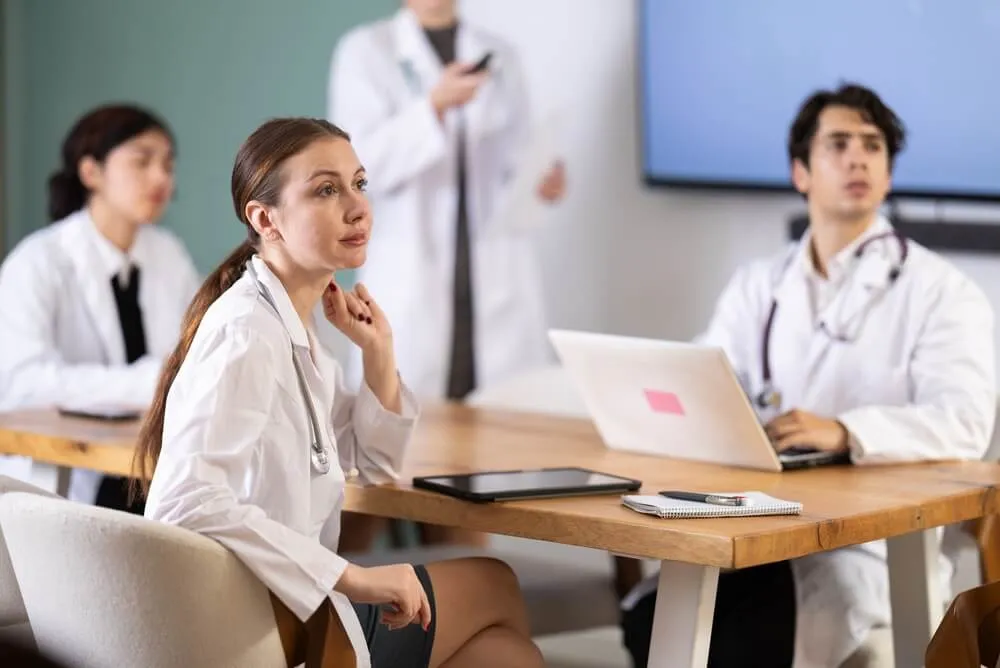 Interested medic student or doctor sitting at table discussing ideas and watching presentation during meeting in bright office