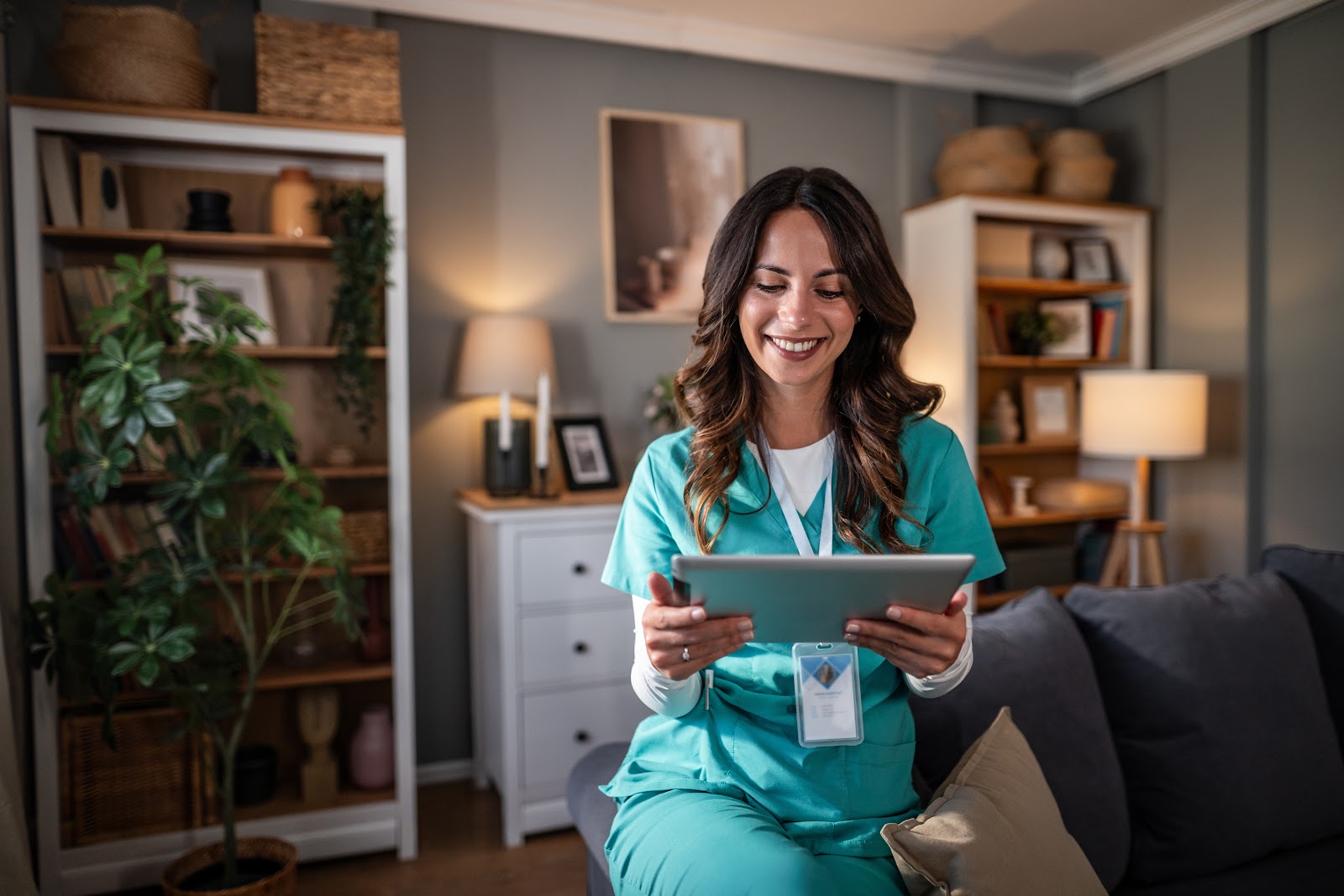 Healthcare professional in scrubs sitting on a couch, conducting a virtual consultation on a tablet