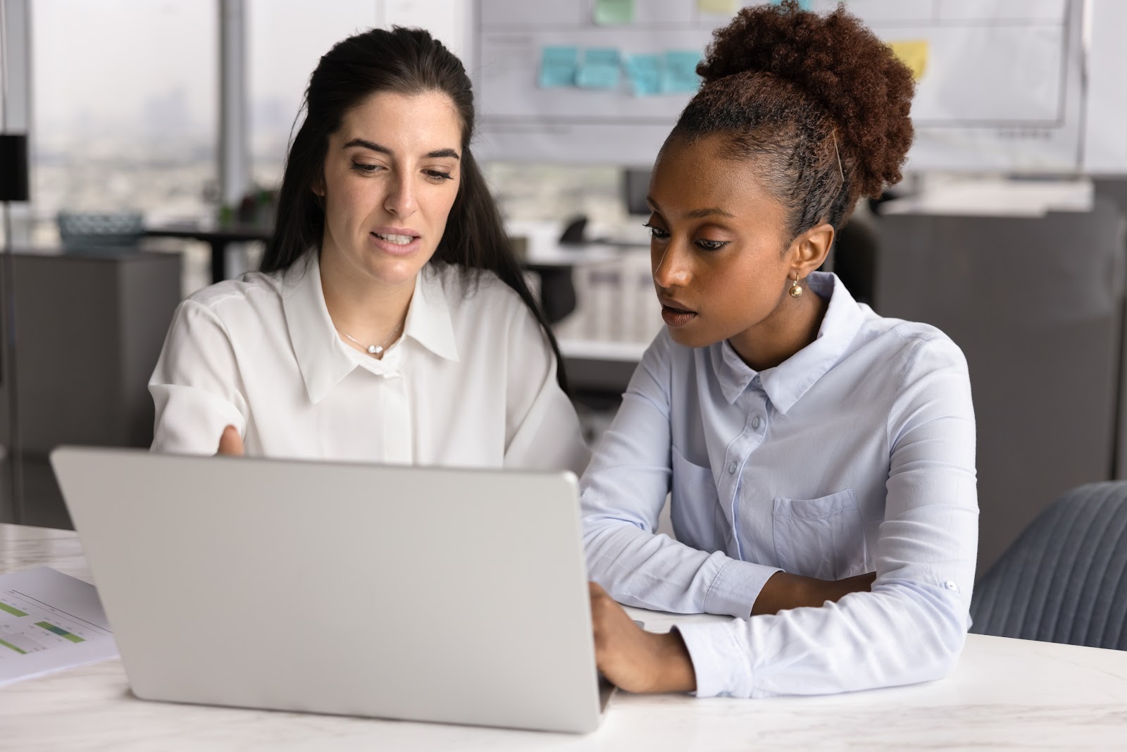 Smiling female mentor at an office desk explaining a report to a young coworker