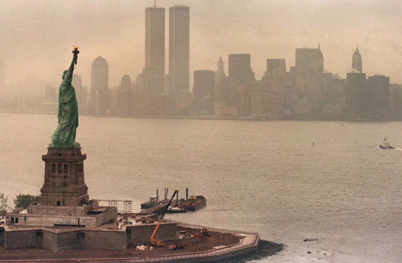 View of the Statue of Liberty with the New York City skyline and the Twin Towers in the background on a hazy day.