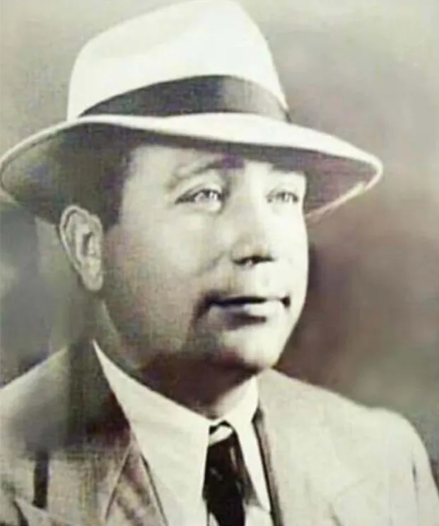 Black and white portrait of a man in a suit and tie wearing a fedora hat, looking slightly to the right.