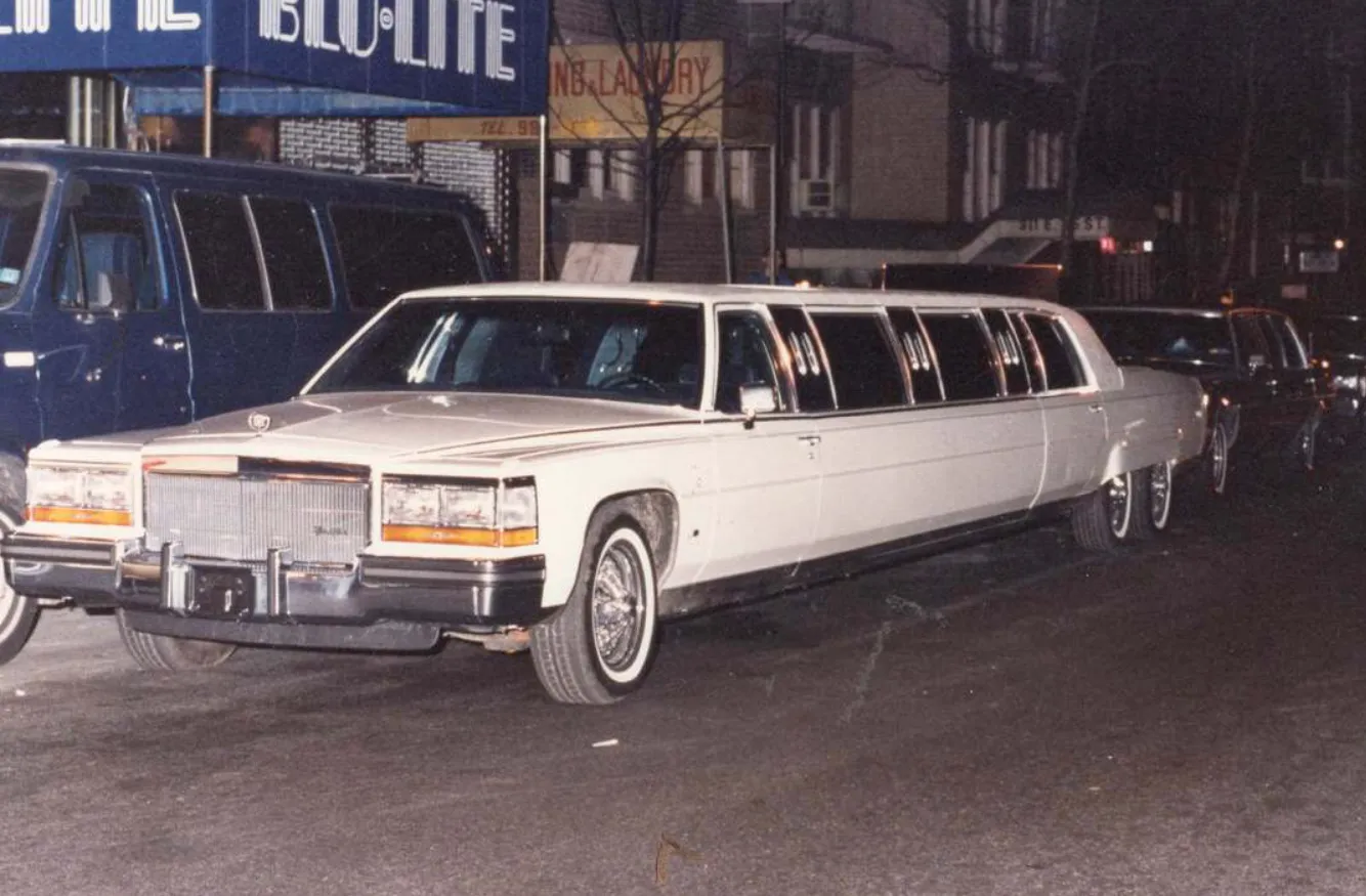 White stretch limousine parked on a city street at night with other vehicles nearby.