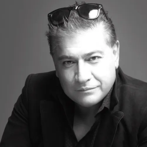 Black and white portrait of a man with short hair wearing sunglasses on his head and a dark jacket, smiling slightly.