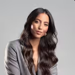 Portrait of a woman with long dark hair wearing a gray blazer against a plain light background.
