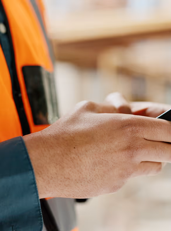 Close-up of a person wearing an orange safety vest using a smartphone.