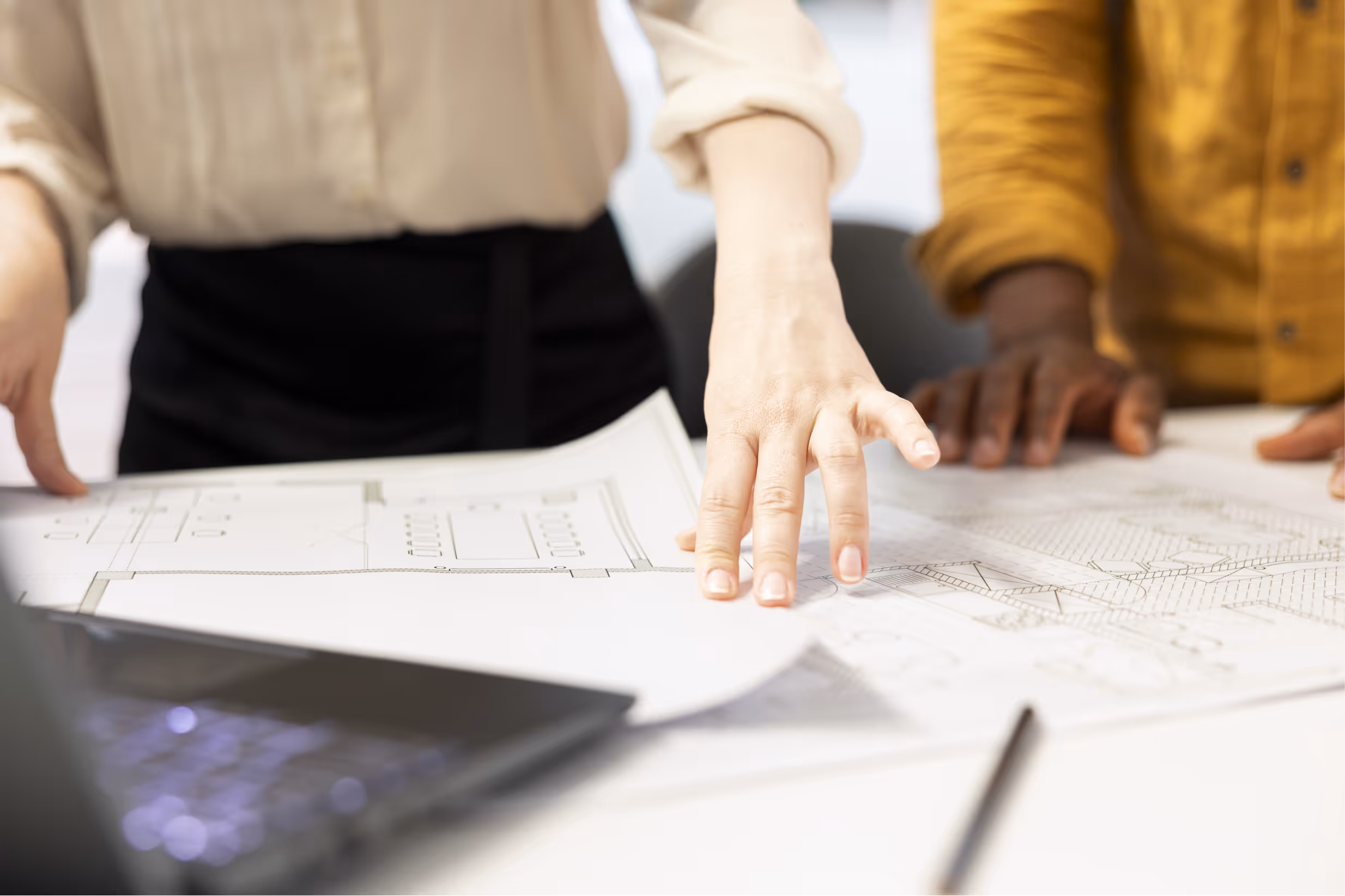 Two people review architectural blueprints on a table with a laptop nearby.