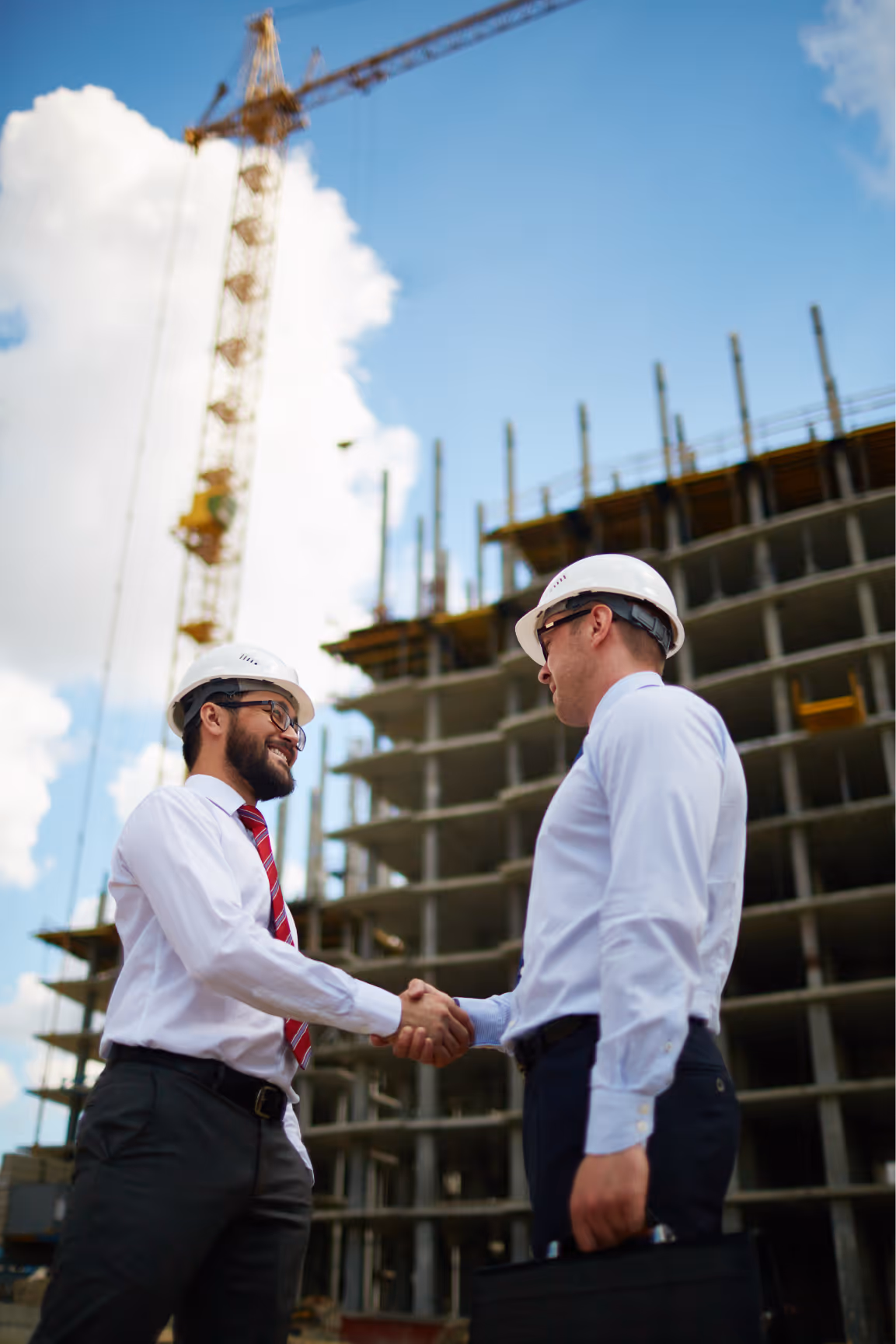 Two construction professionals in hard hats shaking hands at a building construction site.
