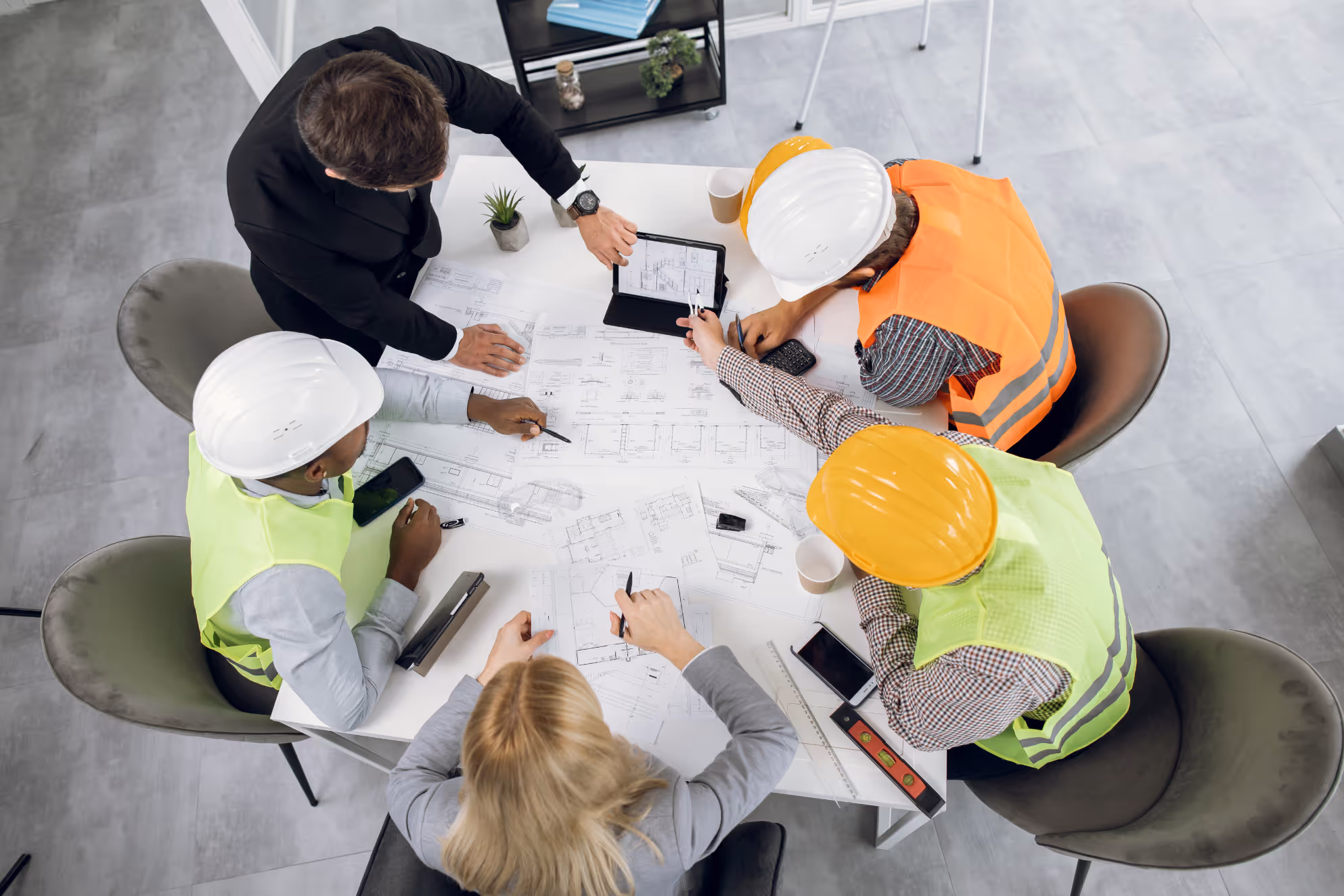 Team of engineers and architect reviewing blueprints and plans around a table with tablets and tools.