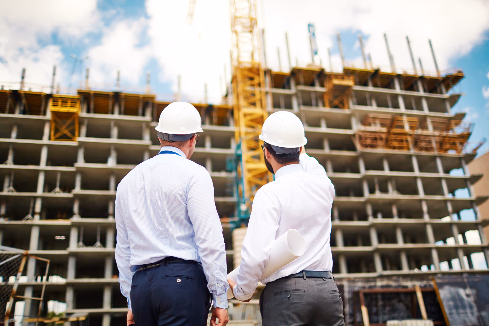 Two engineers wearing white helmets inspecting a building under construction on a sunny day.