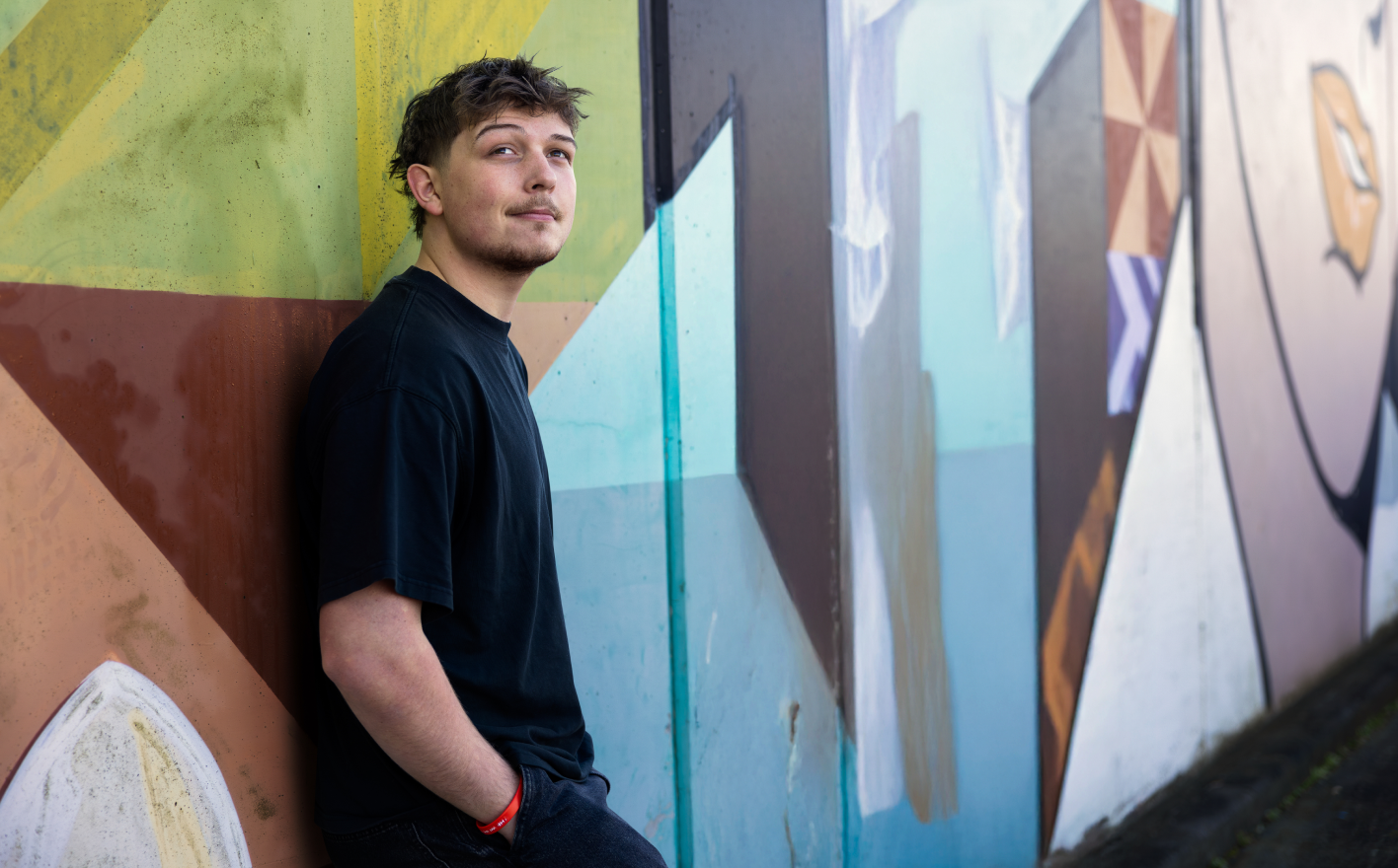 Young man leaning against a colourful painted mural
