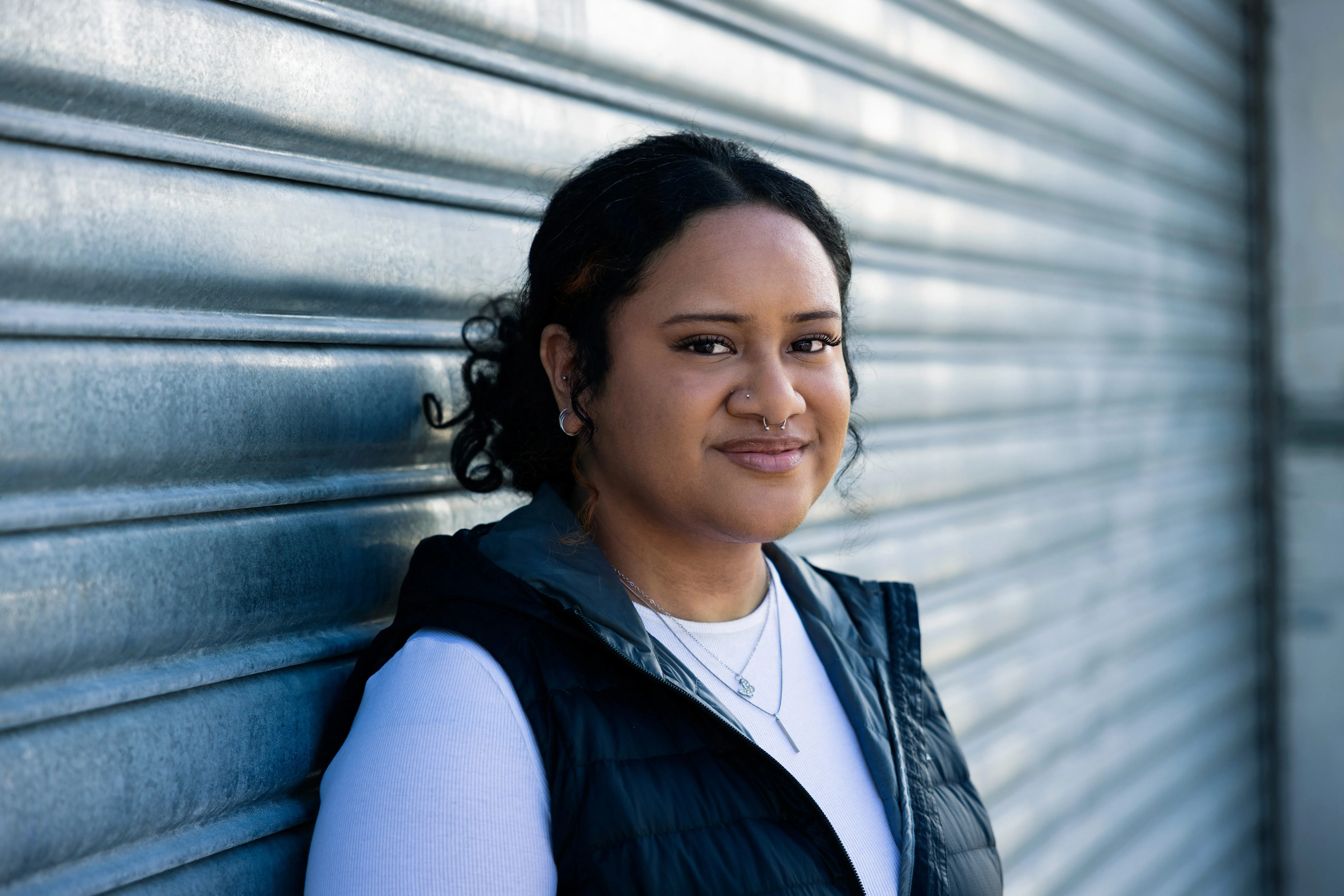 Young woman in a black puffer vest leaning against a corrugated metal roller door