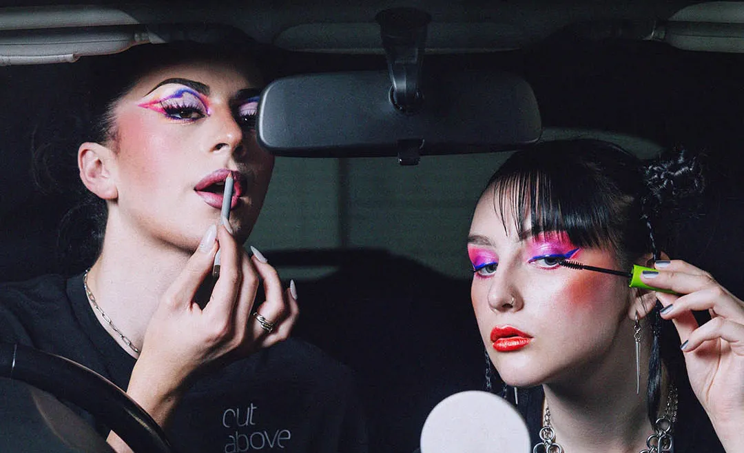 Two young women applying bold colourful makeup in a car