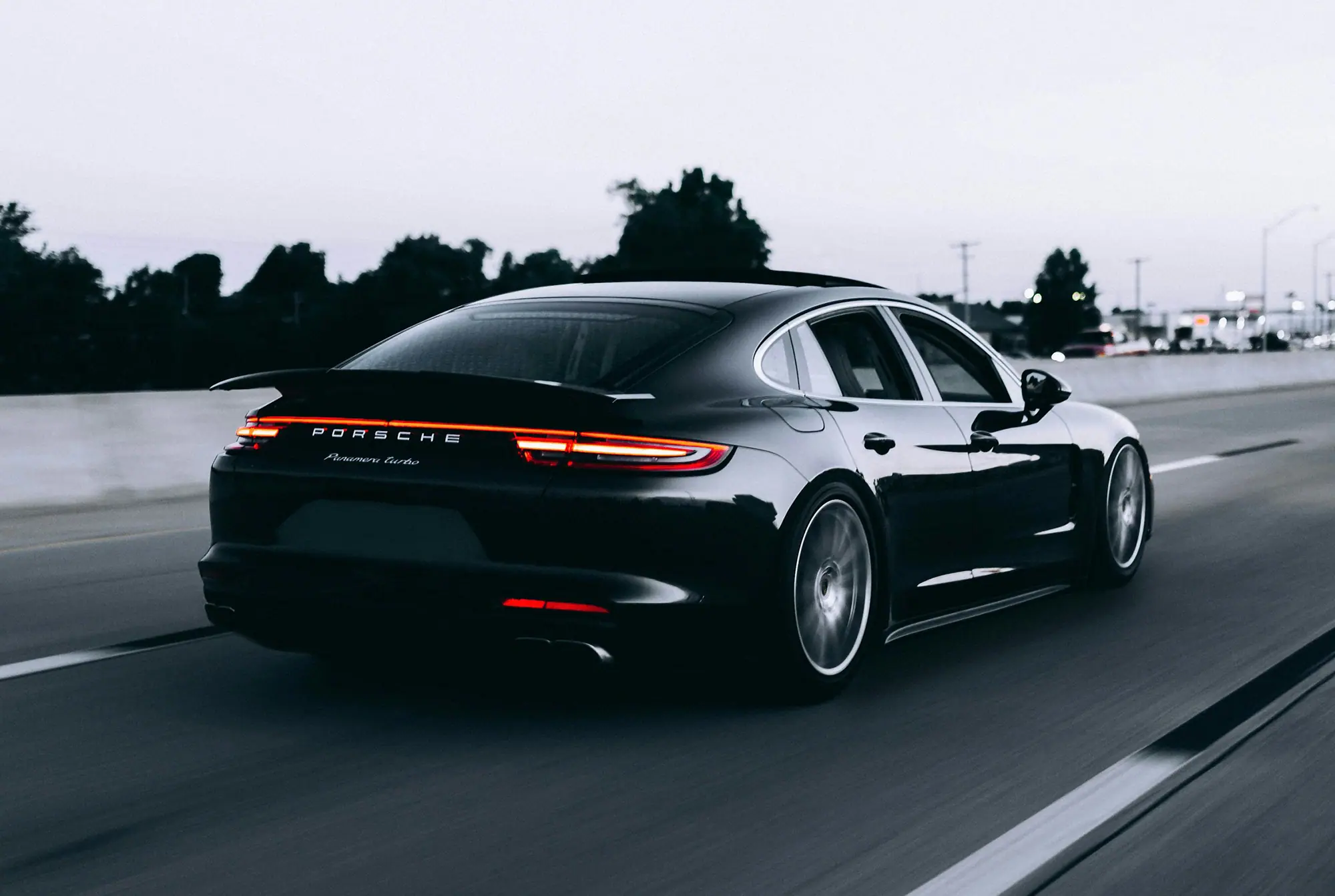 Schwarzer Porsche Panamera Turbo fährt auf einer Straße bei Dämmerung.