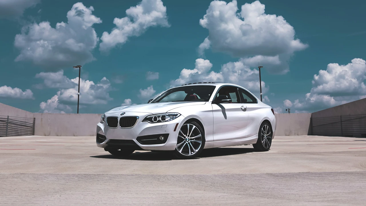 Weißes BMW Coupé auf einem sonnigen Parkdeck vor blauem Himmel mit Wolken.