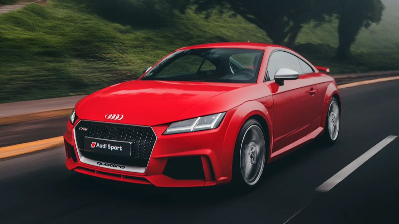 Roter Audi TT Sportwagen fährt auf einer Straße mit grüner Vegetation im Hintergrund.