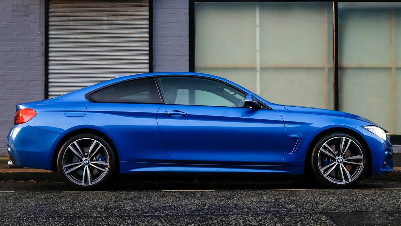Blauer BMW-Sportwagen, seitlich geparkt vor einer Fenster- und Garagentürwand.