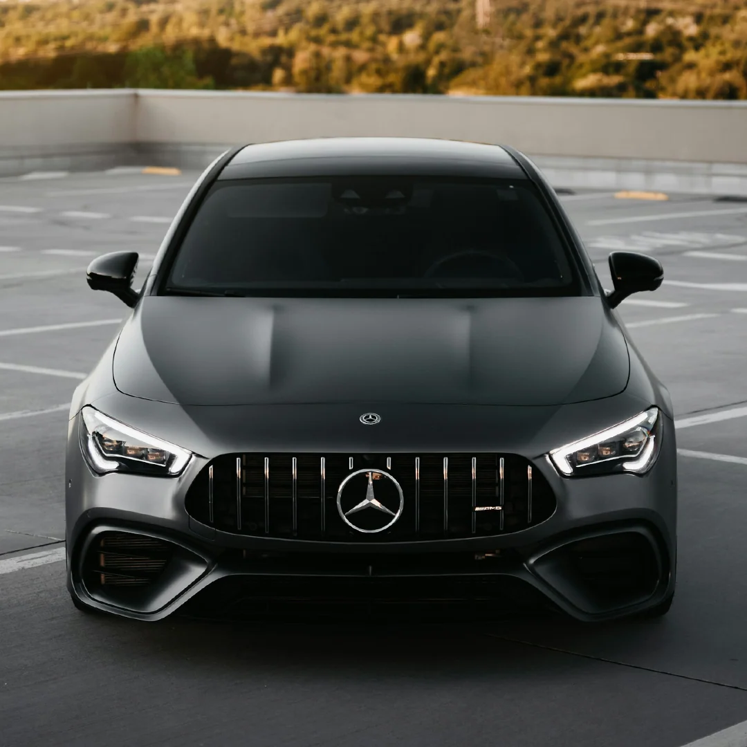 Front view of a sleek black Mercedes-Benz AMG car parked outside with nature in background.
