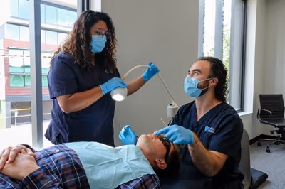 Two dentists wearing masks and gloves examining a patient lying on a dental chair in a clinic.