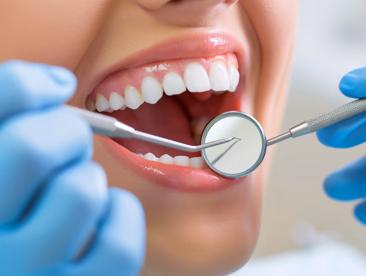 Close-up of a dentist examining a person's open mouth with dental mirror and probe.