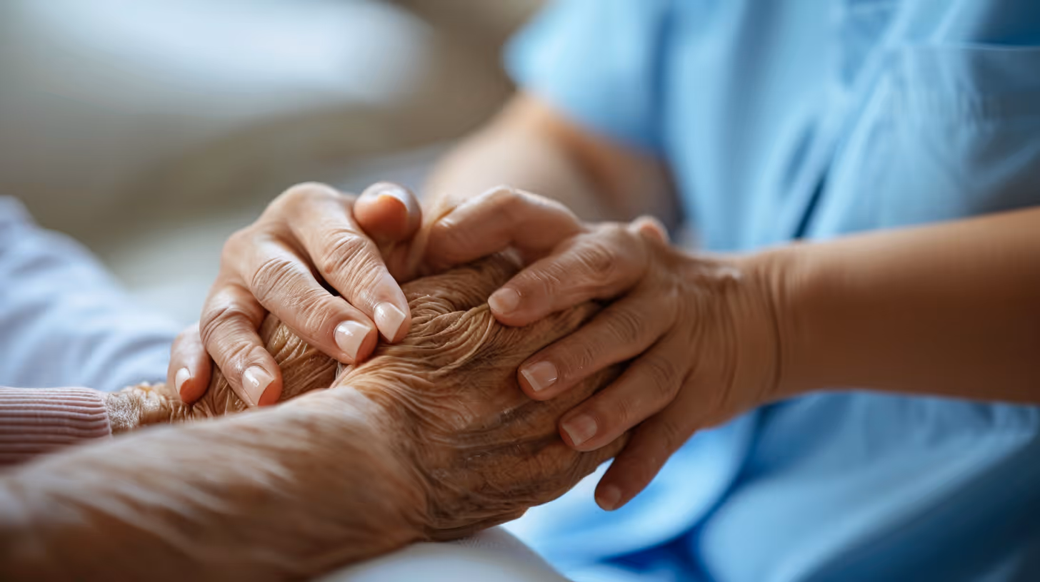 Younger hands gently holding and comforting older wrinkled hands in a caring gesture.