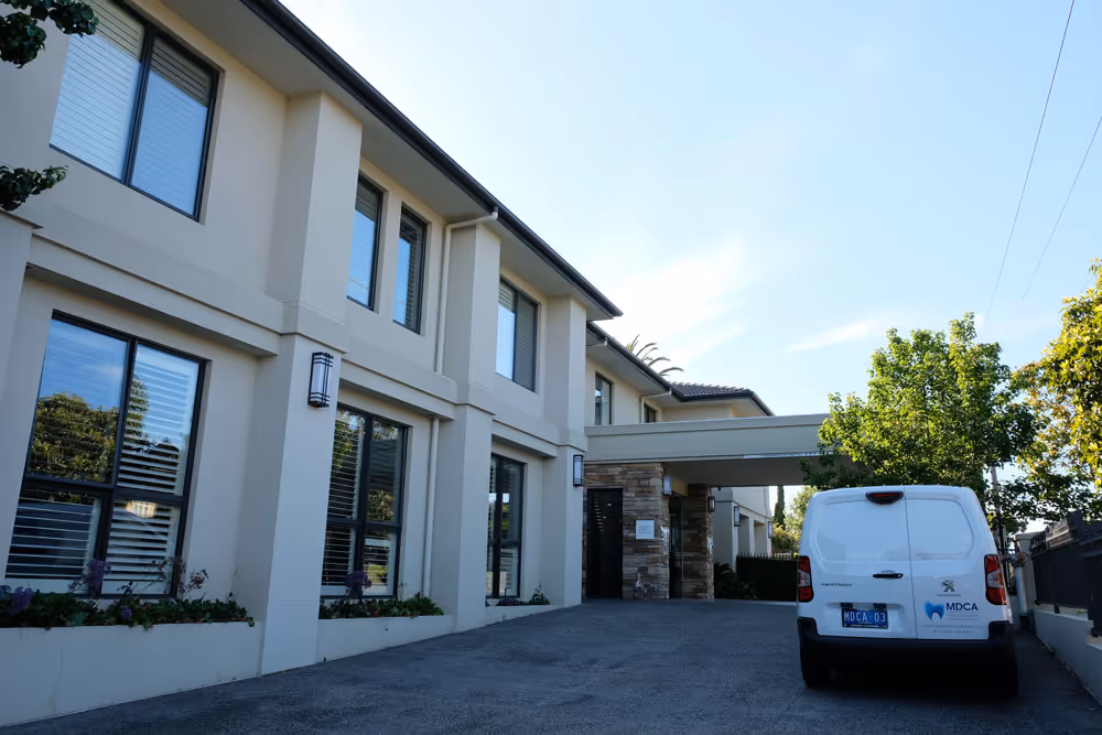 Modern two-story building with large windows and a white van parked on a driveway under a clear sky.
