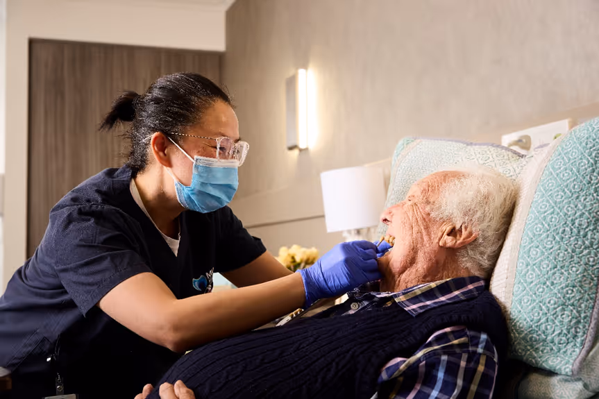 Dentist wearing glasses and mask working on a patient in a bright dental clinic.